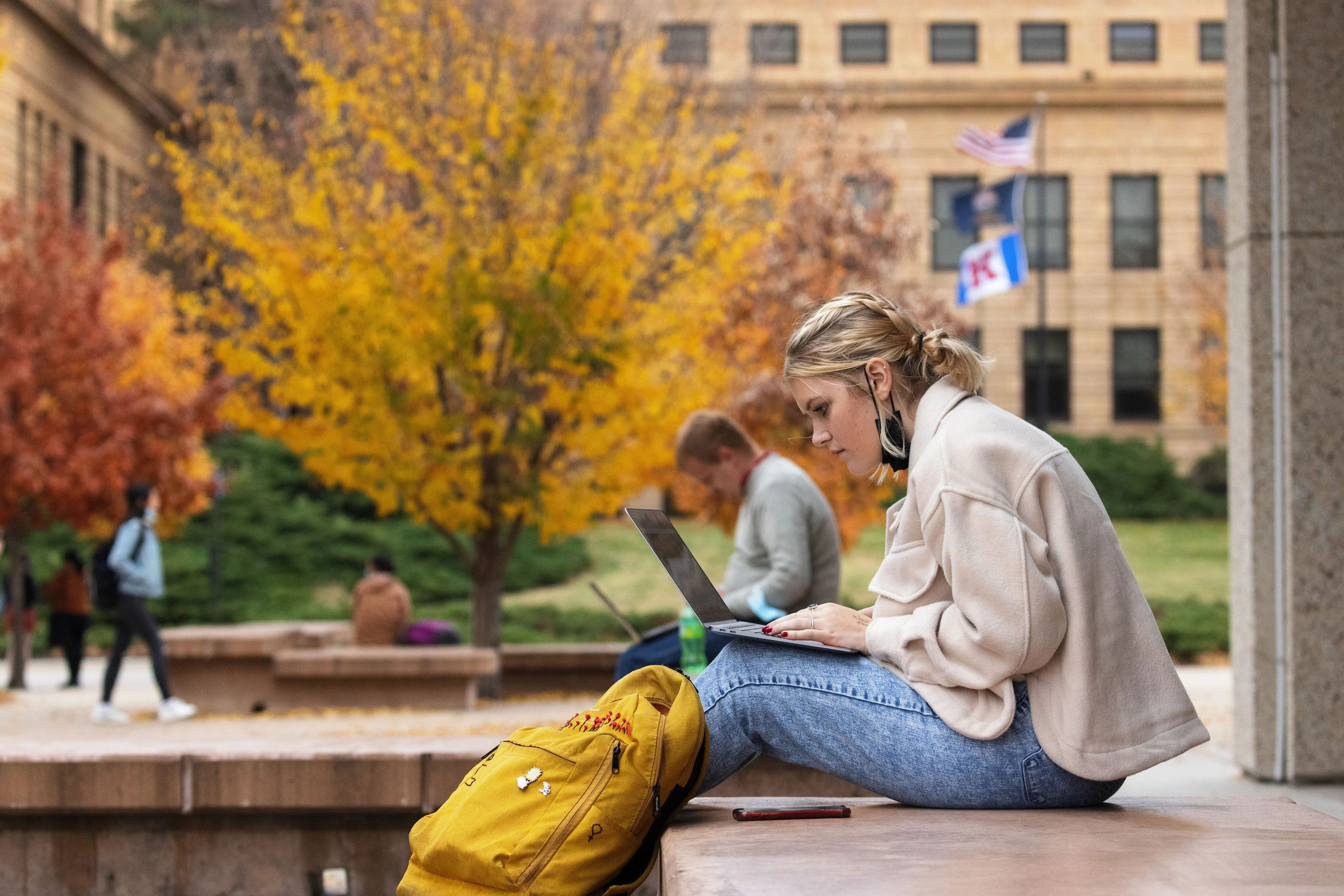 A students sits outside while working on a laptop